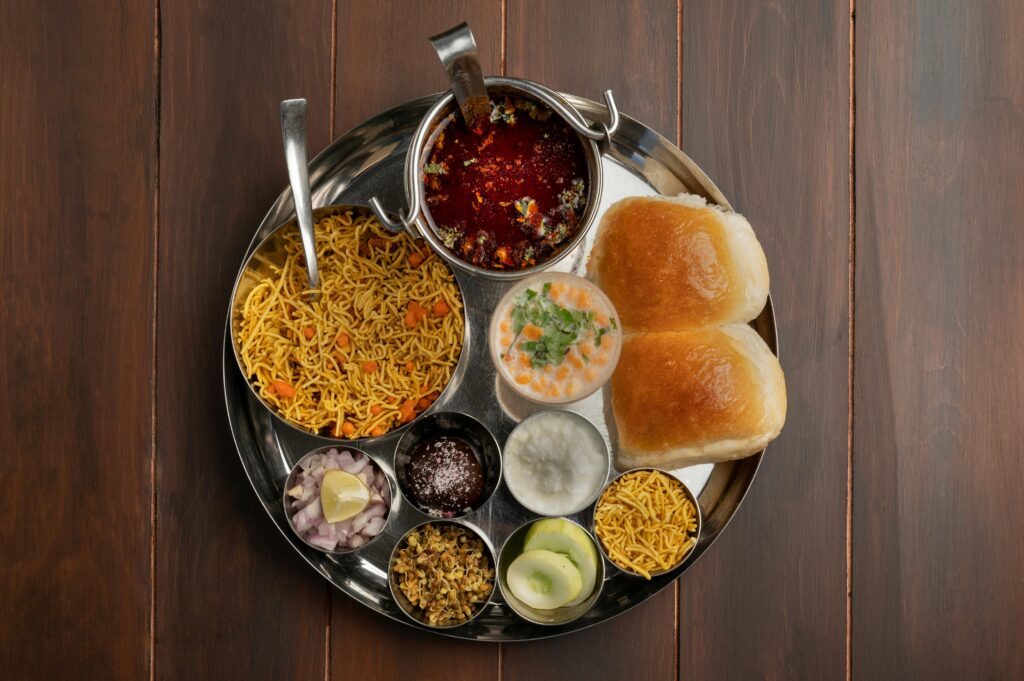A top view of a traditional Maharashtra thali featuring spicy pav bhaji, vegetables, and condiments in Pune, India.
