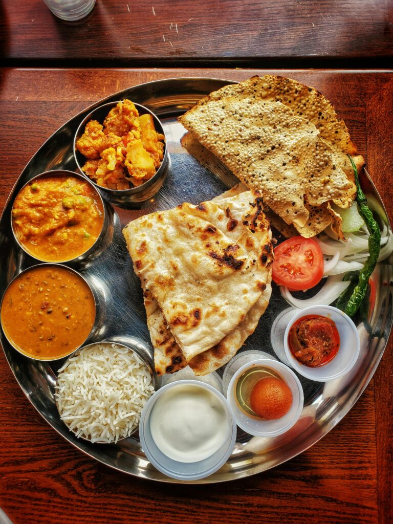 Delicious Indian thali featuring naan, curries, and assorted dips on a tray.